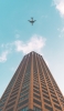 📱茶色い高層ビルと飛行機 iPhone 14 Pro Max 壁紙・待ち受け