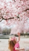 📱桜を見上げる外国人の女の子 iPhone 14 Plus 壁紙・待ち受け