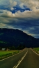 📱雲多い青空と緑の山と舗装された道路 iPhone 13 mini 壁紙・待ち受け