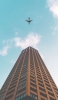 📱茶色の高層ビルと青空と飛行機 iPhone 12 Pro 壁紙・待ち受け